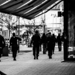 Människor och poliser som promenerar på en stadstrottoar med träd och byggnader runtomkring.