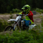 Motocrossåkare i färgglada kläder kör genom grön skogsmark.