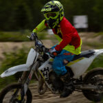 En motorcyklist på grusväg i skog, klädd i färgglada kläder och skyddsutrustning.
