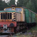 Ett gammalt diesel-lokomotiv med grön vagn på järnväg omgiven av tät skog.