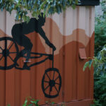 Cyklistmålning på container med berg i bakgrund, omgiven av grönska.