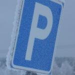 Blå parkeringsskylt täckt av frost i en snöig och dimmig vintermiljö.