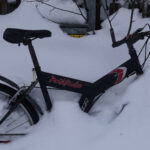 Cykel delvis täckt av snö, med synligt hjul och ram i snöig omgivning.