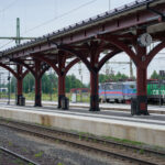 Järnvägsstation med plattformar, Green Cargo-lok, tak med klocka, skog i bakgrunden.
