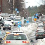 Vintergata med trafik, snötäckta trottoarer, bilar i kö, trafikskyltar och polisbil.